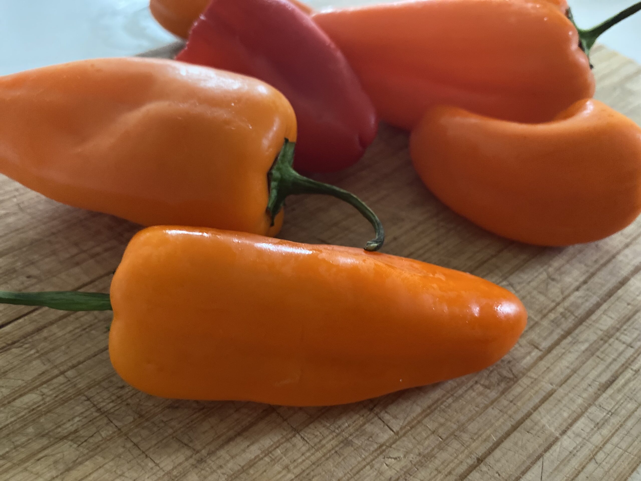 Fresh orange chili peppers on a wooden cutting board, showcasing their vibrant color and smooth texture, ideal for cooking or garnishing.